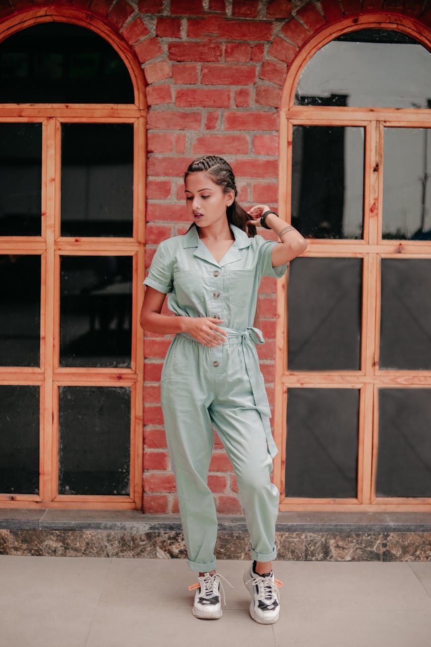 Stylish woman posing in a green jumpsuit against a rustic brick wall.